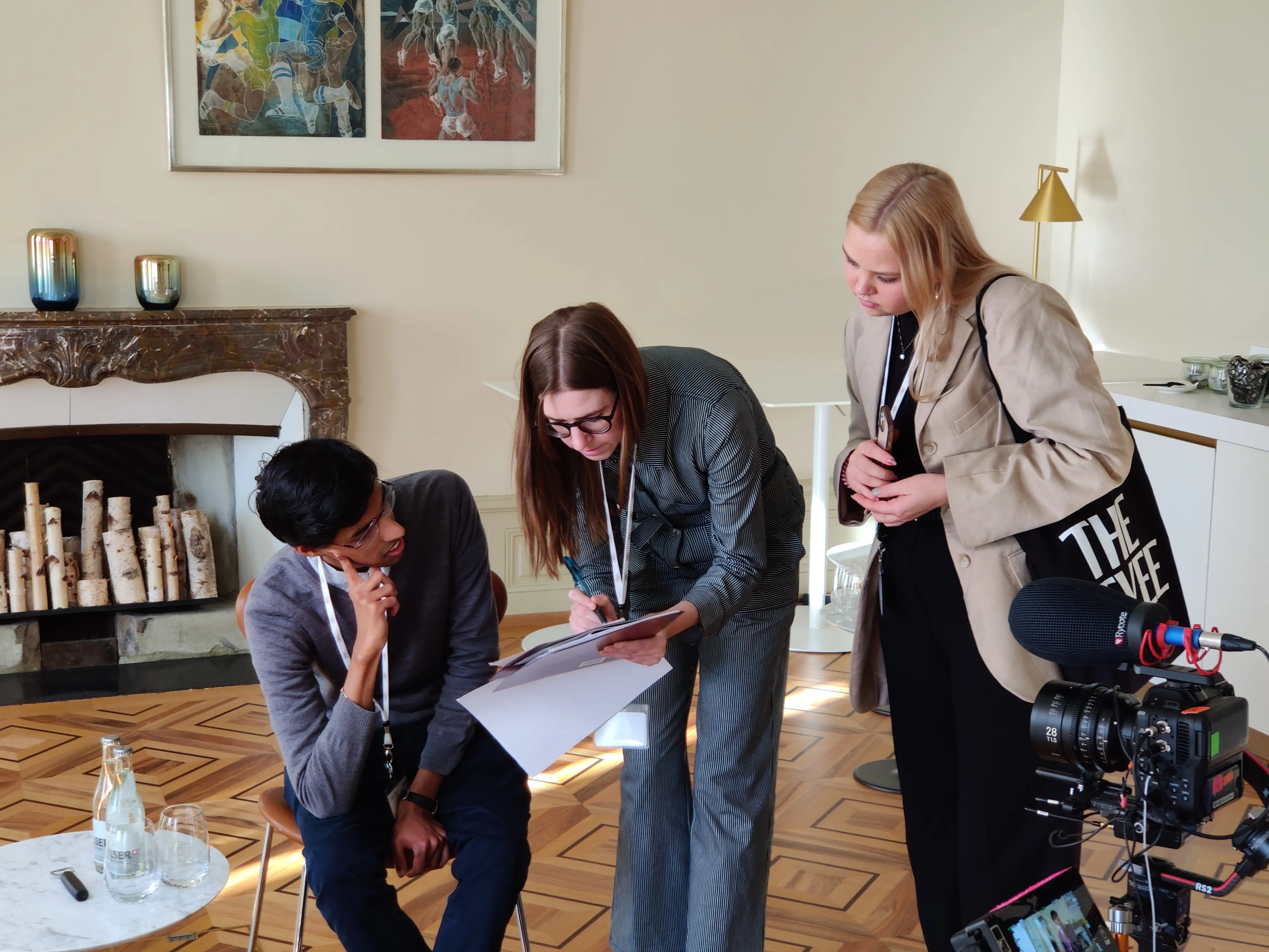A woman reviewing production and interview notes with students, with a camera in the foreground.